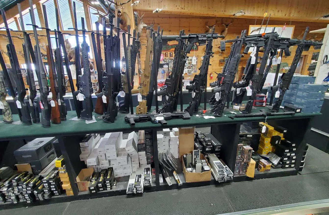 Gun store display with rifles on wall rack and ammunition boxes on shelves below.